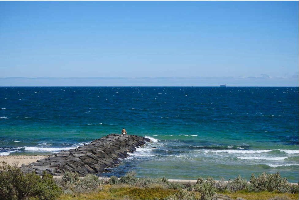 Young man sits on a rock near the ocean contemplating the meaning of life.