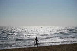 Man walking alone on Melbourne beach at sunset, lost in thought